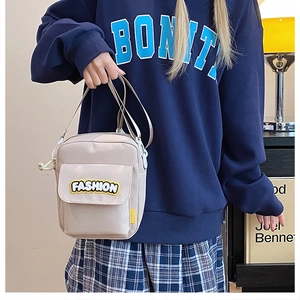 Detail of beige nylon crossbody bag with Fashion patch shown on a navy sweatshirt