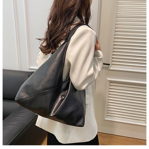 Detail of a large black soft leather tote bag on model showing stitched seams and hobo shape