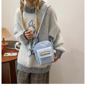 Detail view of a light blue nylon crossbody bag with fashion embroidery and adjustable strap