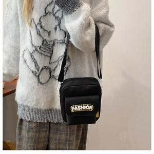 Close-up of black crossbody bag with yellow FASHION patch and white buckle on model