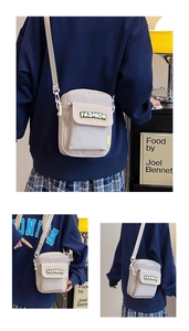 Detail of a beige canvas crossbody bag featuring a yellow Fashion patch and adjustable strap