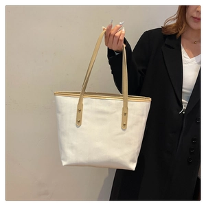 Dettaglio borsa tote in tela bianca con manici in pelle marrone e rivetti dorati