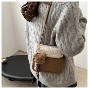 Detail of suede crossbody bucket bag with plush lamb wool trim and bear charm accessory