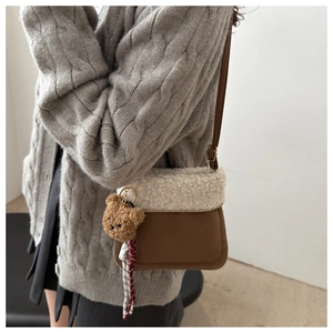 Detail of suede crossbody bag featuring plush fleece flap and a small bear charm