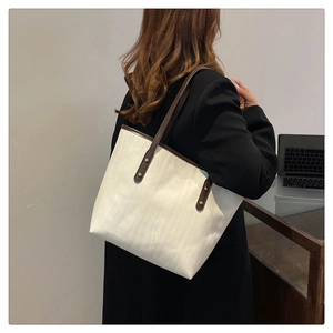 Dettaglio della grande borsa tote in tela con manici in pelle marrone e rivetti in metallo