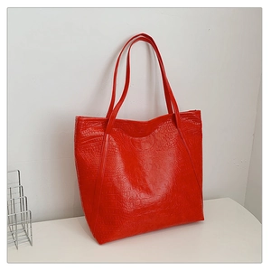 Macro shot of large red tote bag featuring glossy crocodile texture and long shoulder straps