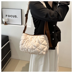 Quilted off-white puffy shoulder bag with adjustable brown strap shown on a model