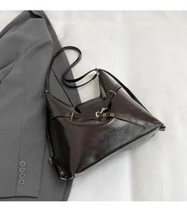 Detail of dark brown glossy leather tote with metal buckle placed on a grey blazer
