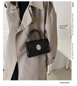 Detail of black crocodile texture leather bag with silver metal lock and chain strap