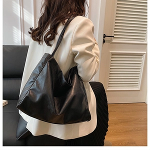 Model wearing a large black textured faux leather tote bag in a modern indoor setting