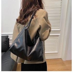 Detailed view of a large black leather tote bag worn by a model in a brown suit blazer