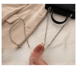 Detail of silver oval metal chain strap on black crocodile pattern leather handbag