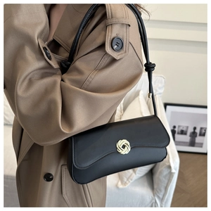 Detail of a black leather shoulder bag featuring a golden woven circular buckle design