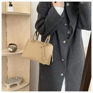 Detail view of a beige matte leather shell bag held by a model in an elegant lifestyle setting