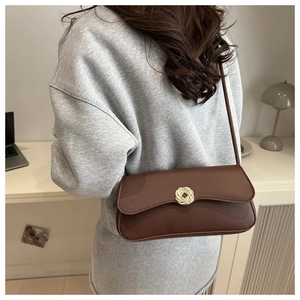Brown leather underarm bag with gold knot buckle shown on model in a home office setting