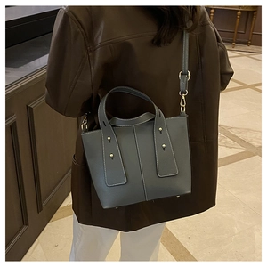 Sac seau en cuir bleu-gris avec surpiqûres blanches porté par un mannequin en extérieur