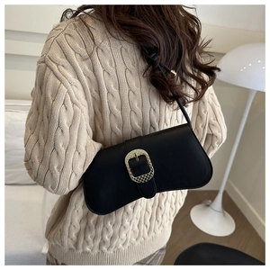 Sac à bandoulière en cuir noir avec boucle dorée, porté sur un pull en maille beige