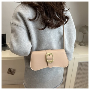 Détail d'un sac porté épaule beige avec boucle dorée texturée sur un modèle minimaliste