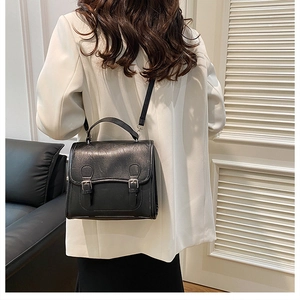 Rear view of a model wearing a classic black British style satchel with twin buckles