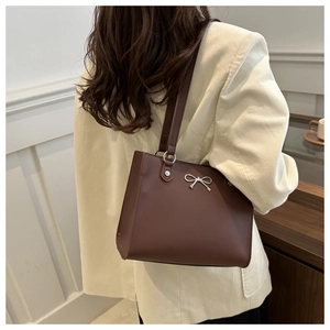 Detail of dark brown faux leather tote bag with silver bow accent on beige coat