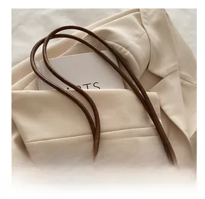 Dettaglio di una borsa tote marrone con manici in pelle e scritta Fashion su un blazer