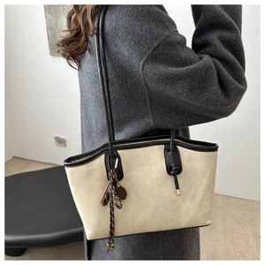 Dettaglio borsa tote beige con finiture nere e ciondolo a nappa elegante sul fianco