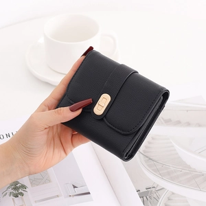 Close-up of black textured leather wallet with gold buckle held in a lifestyle setting
