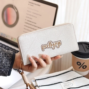 Close-up of a beige woven pattern long wallet with gold zipper held by a model