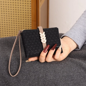Detail of black knit texture wallet with golden leaf clasp and wrist strap being held