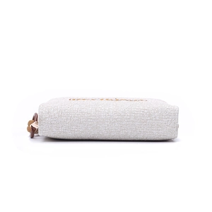 Détail de pochette en toile crème avec surpiqûres en losanges et dragonne marron
