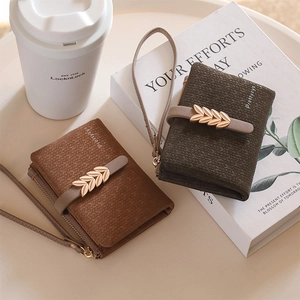 Close-up of two bifold zip wallets with leaf-shaped gold hardware and wrist straps