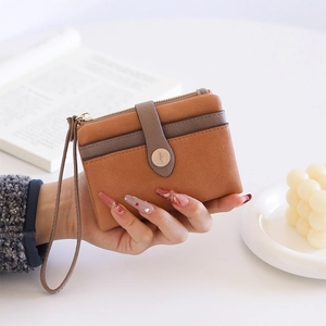 Detail of a brown PU leather compact wallet with zip and strap held in hand