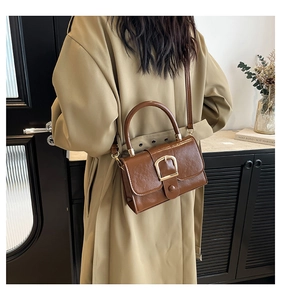 Lifestyle shot of a woman in beige coat holding a brown vintage leather handbag with gold buckle