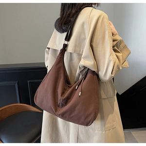 Gros plan sac à bandoulière en daim marron avec surpiqûres blanches et trench-coat