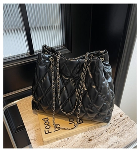Detail of black quilted leather tote bag with metal chain strap on marble surface