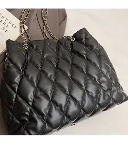 Close-up of black quilted leather tote bag featuring elegant gold chain woven straps
