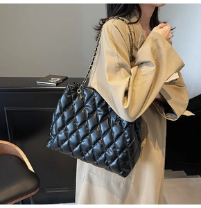 Detail showing high-capacity black quilted tote bag with chain strap worn with a beige coat