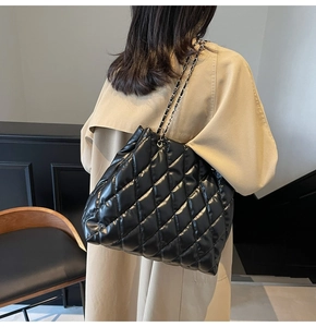 Macro shot of black quilted tote bag with chain strap worn on shoulder for daily commute