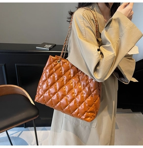 Detail of caramel leather quilted tote bag with gold chain strap worn by a model
