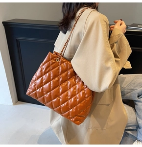 Detail of caramel quilted tote bag with golden metal chain strap on model shoulder