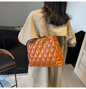 Detail of a brown quilted leather tote bag featuring a gold metal chain strap for women