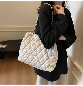 Detail of white quilted tote bag with gold chain strap shown on model's shoulder