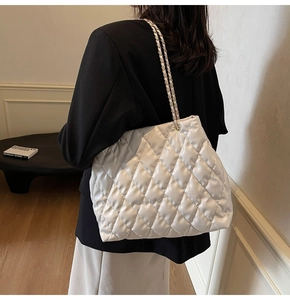 Detail of white quilted shoulder bag with woven metal chain strap on model shoulder