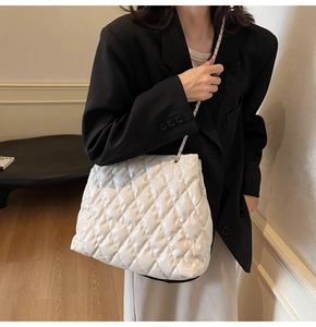Close-up of white quilted tote bag with metal chain strap on a black blazer