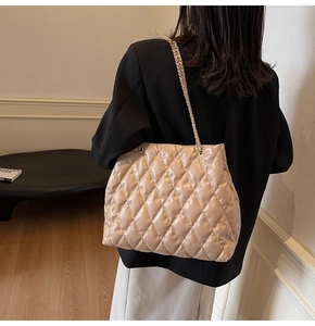 Close-up of beige quilted chain shoulder bag worn by model in a minimalist room