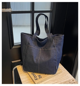 Detail of dark blue denim tote bag with large front pockets on a textured surface