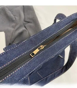 Detailed close-up of smooth gold metal zipper on navy blue denim tote bag with contrast stitching