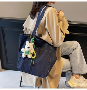 Detail of blue denim tote bag with white puppy plush charm and black fashion side label
