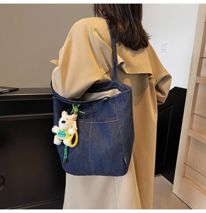 Detail of dark blue denim tote bag with contrast stitching and plush dog charm