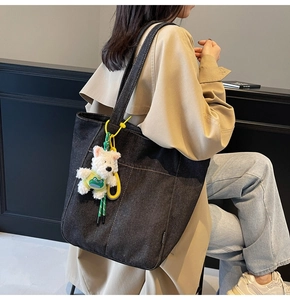 Detail of a large black denim tote bag with a cute white dog plush keychain